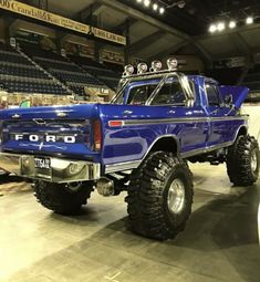 a large blue truck with big tires on display in a showroom or convention hall