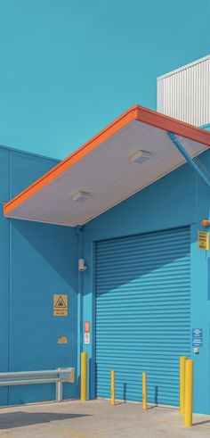 an empty parking lot next to a blue building with yellow and orange posts on it