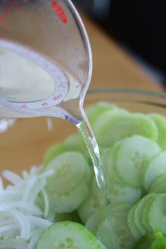 the cucumbers have been cut up and are being poured into a bowl with water