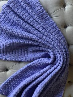 a blue knitted blanket laying on top of a white couch