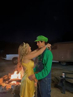 a man and woman standing in front of a campfire with their arms around each other