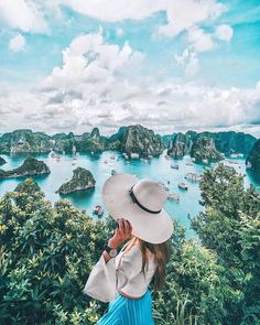 a woman wearing a hat looking out over an island in the ocean with boats on it