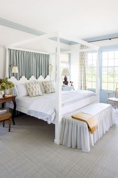 a white bed sitting in a bedroom next to a window with curtains on the windowsill