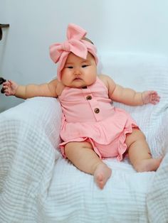 a baby sitting on top of a bed wearing a pink dress