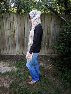 a person standing in the grass wearing a crocheted scarf over their head and hood