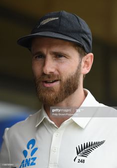 a man with a beard wearing a white shirt and black hat is looking off to the side