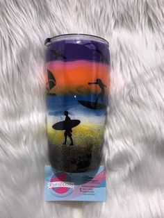 a purple and blue tumbler cup with a surfer on the beach at sunset in front of white fur