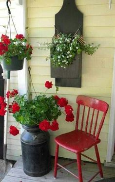 two red chairs sitting next to each other on a porch with flowers hanging from the wall