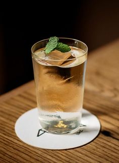 a close up of a glass on a table with ice and a mint sprig