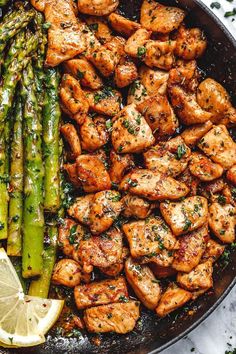 chicken and asparagus in a skillet with lemon wedges