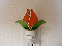 an orange and green flower sitting on top of a white wall outlet with a light switch