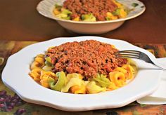 a white plate topped with pasta covered in meat and sauce next to a bowl of cheese