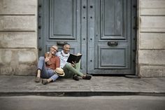 two people sitting on the ground in front of an open door and reading a book