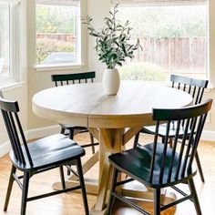 a dining room table with four chairs and a vase on top of it in front of a window