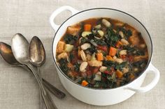 a white bowl filled with soup next to two spoons on top of a table