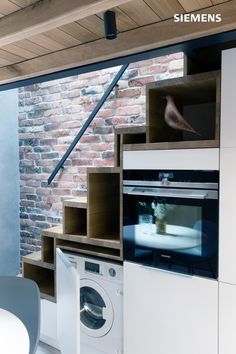 an oven and washing machine in a room with brick walls, white cabinets and flooring