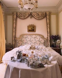 a white bed topped with lots of dishes and cups next to a chandelier