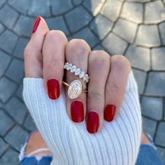 a woman's hand with red nail polish holding a diamond ring