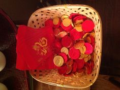 a basket filled with lots of red and gold coins next to an orange napkin on top of a table