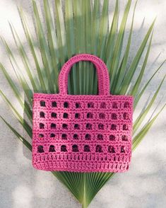 a pink crocheted bag sitting on top of a palm tree branch next to a white wall