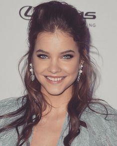 a woman with long hair and blue eyes smiles at the camera while wearing earrings on her head