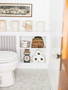 a white toilet sitting in a bathroom next to a shelf filled with books and cups