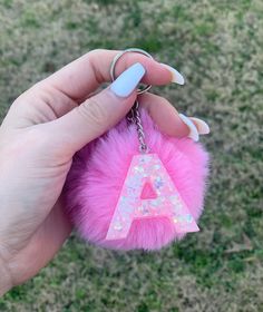 a pink furry keychain that has the letter a on it and is being held by a hand