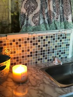 a lit candle sitting on top of a counter next to a sink