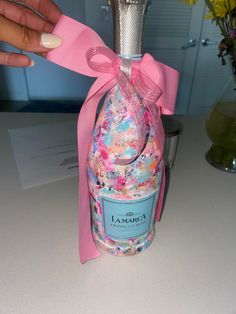 a bottle with a pink ribbon tied around it sitting on a table next to flowers