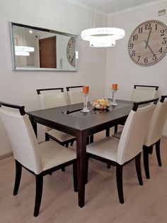 a dinning room table with chairs and a large clock on the wall behind it