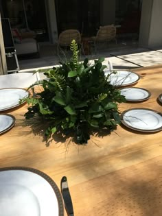 the table is set with white plates and greenery