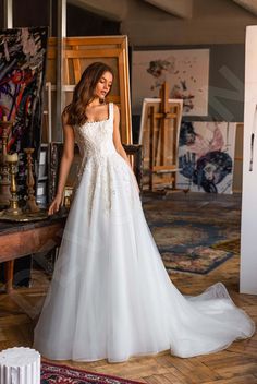 a woman in a white wedding dress standing next to an easel with paintings on it