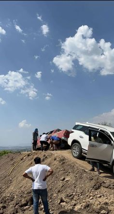 two people standing on top of a hill next to a car