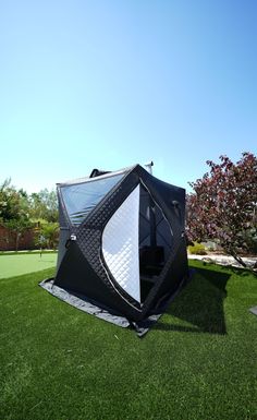 a black and white tent sitting on top of a lush green field next to a tree