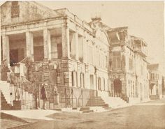 an old black and white photo of people standing in front of two large buildings with stairs leading up to them