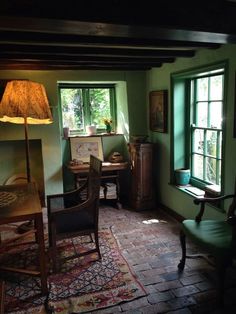 a room with green walls and wooden furniture in front of a large window that has a lamp on top of it