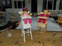 two dolls sitting in high chairs on top of a table