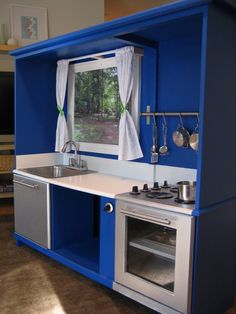 a blue and silver kitchen with an oven, sink, and window in the corner