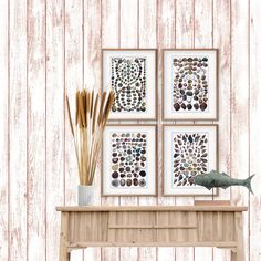 three framed art pieces on a wooden wall above a table with a vase and reeds