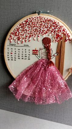 a pink dress is hanging on the wall next to a cross - stitch calendar with red and white beads