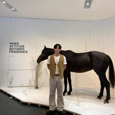 a man standing next to a black horse on top of a snow covered ground in front of a white wall