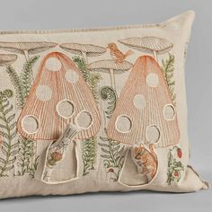 an embroidered pillow with mushrooms and plants on the front, along with a bird perched on it