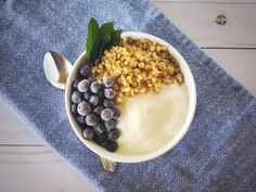 a bowl filled with cereal and blueberries on top of a blue cloth next to a spoon