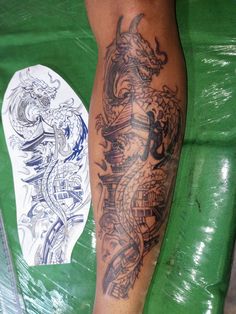 a man with a dragon tattoo on his leg next to a white plate and green table cloth