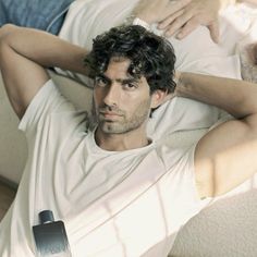 a man laying on top of a bed next to a bottle of cologne in his hand