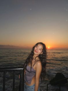 a woman standing on top of a balcony next to the ocean at sunset or dawn