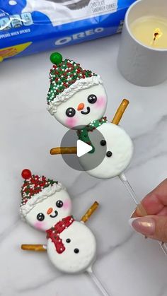 three marshmallow snowmen on sticks with a candle in the background