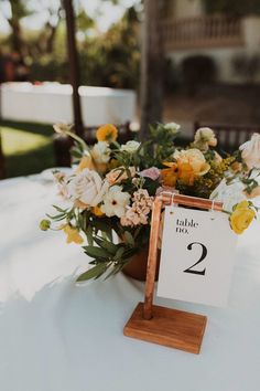 a table number sign with flowers and greenery on it at an outdoor wedding reception