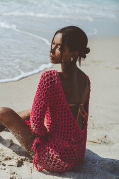 a woman sitting on the beach with her feet in the sand and looking off into the distance