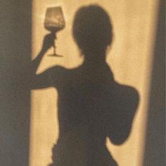 the shadow of a woman holding a wine glass in front of her face and arm